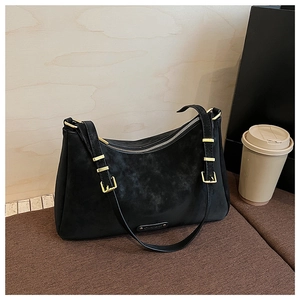 Detail of black matte suede shoulder bag with gold metal buckle on a textured cushion