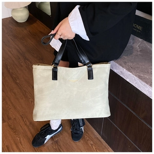 Detail of light green tote bag with black leather straps and gold ring hardware