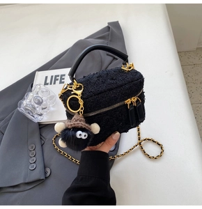 Detail of black tweed box bag featuring gold chain strap and fuzzy eye pendant accessory