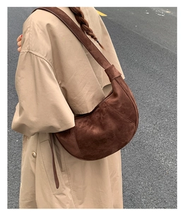 Detail of a dark brown crescent suede shoulder bag worn with a khaki autumn trench coat
