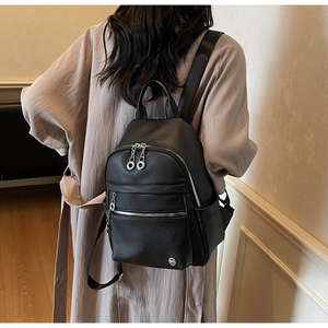 Rear view of a model wearing a black pebbled leather backpack with silver zippers