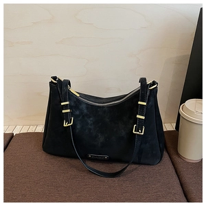Detail of matte black crossbody bag with gold hardware on textured brown surface