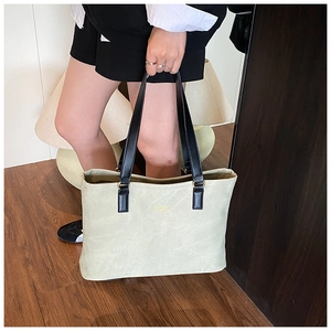 Detail of sage green tote bag with gold logo and long black shoulder straps