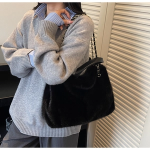 Detailed view of black plush tote bag with gold chain strap worn on grey sweater