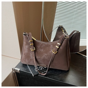 Detail view of dark brown suede shoulder bag showing golden zipper and metal logo plate