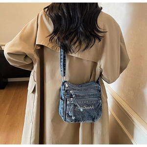 Detail of vintage blue denim crossbody bag featuring multi-pocket zippers and embroidery