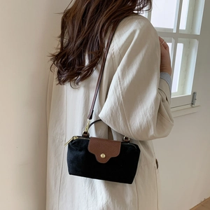 Black suede crossbody bag with brown leather flap shown on a model in a minimal setting
