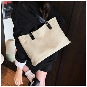 Beige leather tote bag with black strap worn by model on shoulder for size display