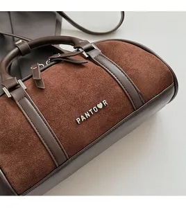 Detalle del bolso Boston retro de ante marrón con ribete de cuero y logotipo de marca