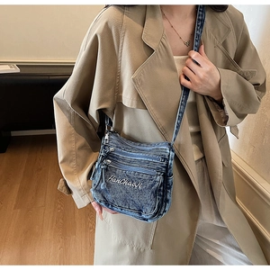 Detail of blue denim crossbody bag with multiple zippers and white letter embroidery