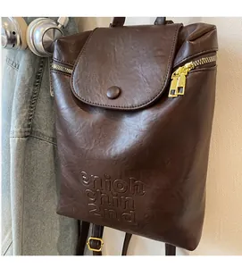 Détail du sac à dos en similicuir marron avec texte en relief et fermetures éclair dorées