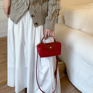 Detail of red faux suede crossbody bag with gold hardware and snap closure on white dress