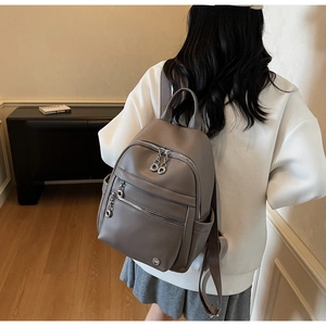 Detail of grey pebbled leather backpack with silver zippers worn in a modern room