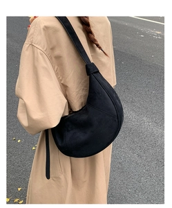 Close-up of black suede moon bag with wide strap and metallic buckle detail on camel coat