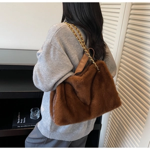 Brown fluffy faux fur tote bag with golden metal chain strap shown on a model