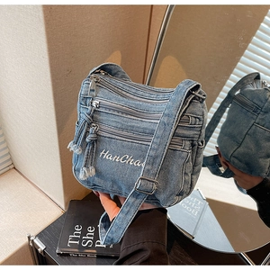 Detail view of washed blue denim crossbody bag with multi-zipper pockets and embroidery