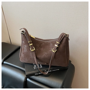 Close-up of deep coffee matte textured shoulder bag with gold buckles on a leather bench