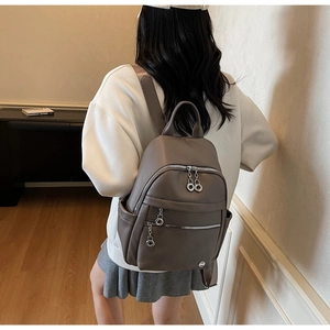 Brown lychee leather backpack with multiple zippers shown on a model in a warm room