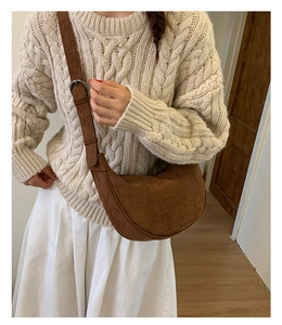 Brown suede crescent moon crossbody bag styled with a beige knit sweater and white skirt
