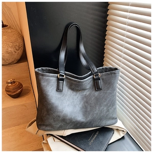 Detail of grey tote bag with textured finish, gold hardware, and sturdy black handles