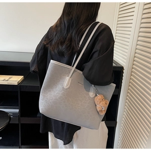 Detail of grey leopard embossed tote bag with plush bear charm and luxury branding