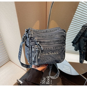 Detail of vintage blue denim crossbody bag featuring multiple zippers and embroidery