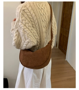 Brown suede crescent bag shown on model with a vintage aesthetic and wide shoulder strap