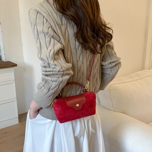 Detail of red suede crossbody bag with gold button closure and model in knitwear
