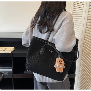 Close-up of leopard print tote bag with brown plush bear charm and metallic logo detail