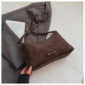 Close-up of deep brown suede shoulder bag with gold hardware and brand metal logo
