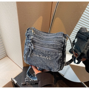 Detailed close-up of a retro blue washed denim crossbody bag with multiple zip pockets