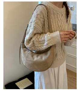 Detail view of a beige crescent suede shoulder bag styled with a retro knit sweater