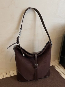 Grand sac hobo marron foncé avec bandoulière nouée et anneau sur fond de bois épuré