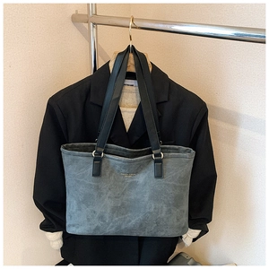 Detail of grey-blue suede tote bag with gold lettering hanging on a suit hanger