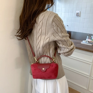 Detail of red faux suede crossbody bag with gold buckle on a minimalist background
