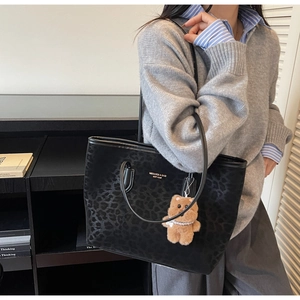 Detail of leopard print tote bag with golden logo and plush bear charm on a model