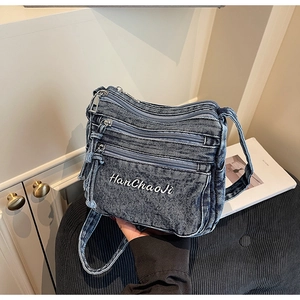 Detailed macro view of denim crossbody bag featuring white embroidery and metal zippers