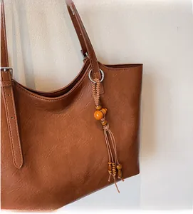 Detail of dark brown leather tote bag featuring ethnic wooden bead tassels and hardware