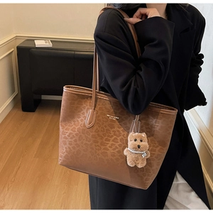 Close-up of leopard print tote bag texture with brand logo and cute plush bear charm