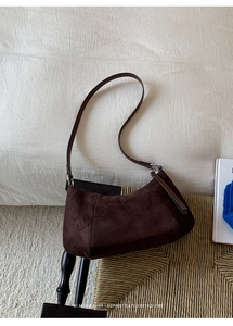 Gros plan d'un sac demi-lune en daim marron posé sur un fond de chaise en rotin tressé