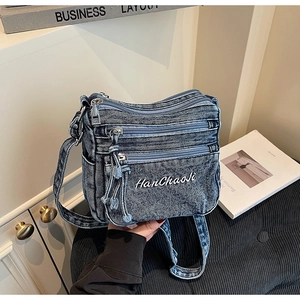Detail of vintage washed blue denim crossbody bag featuring triple front zipper pockets