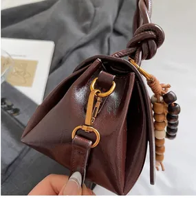 Detail of dark brown glossy leather handbag with vintage gold hook and wood bead charm