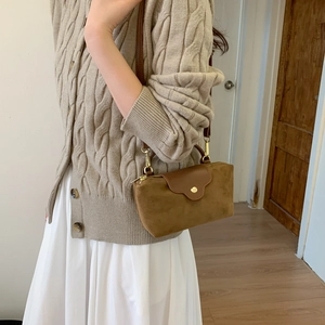 Detail of brown suede crossbody bag with gold hardware worn by model in casual outfit