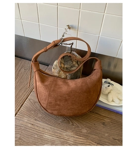 Dettaglio di una borsa a mezzaluna in camoscio marrone con cuciture su piano in legno vintage