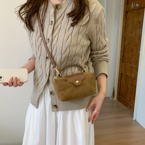 Detailed shot of brown suede mini crossbody bag with gold buckle on a model wearing knitwear