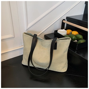 Close-up of a pale green tote bag featuring black shoulder straps and subtle gold lettering