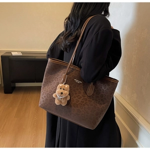 Detail of leopard print tote bag with plush bear charm and brand logo on shoulder strap