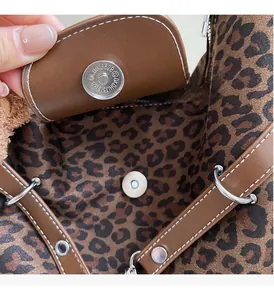 Detailed close-up of brown leather flap with metallic magnetic buckle on leopard print bag