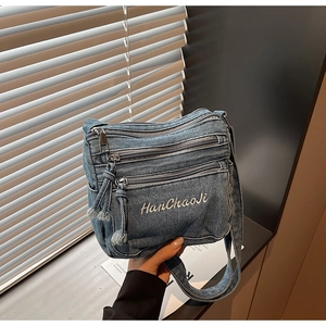 Detailed macro of vintage blue denim crossbody bag featuring triple zipper pockets and logo