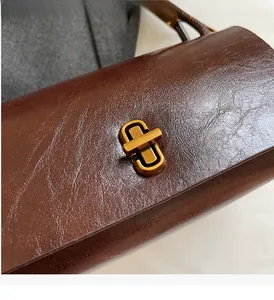 Detail of vintage gold-tone twist lock and dark brown oil-wax leather texture on handbag